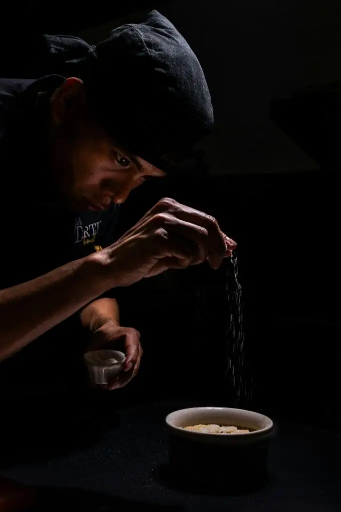 An experienced chef adding sugar to a pot of creme brulee