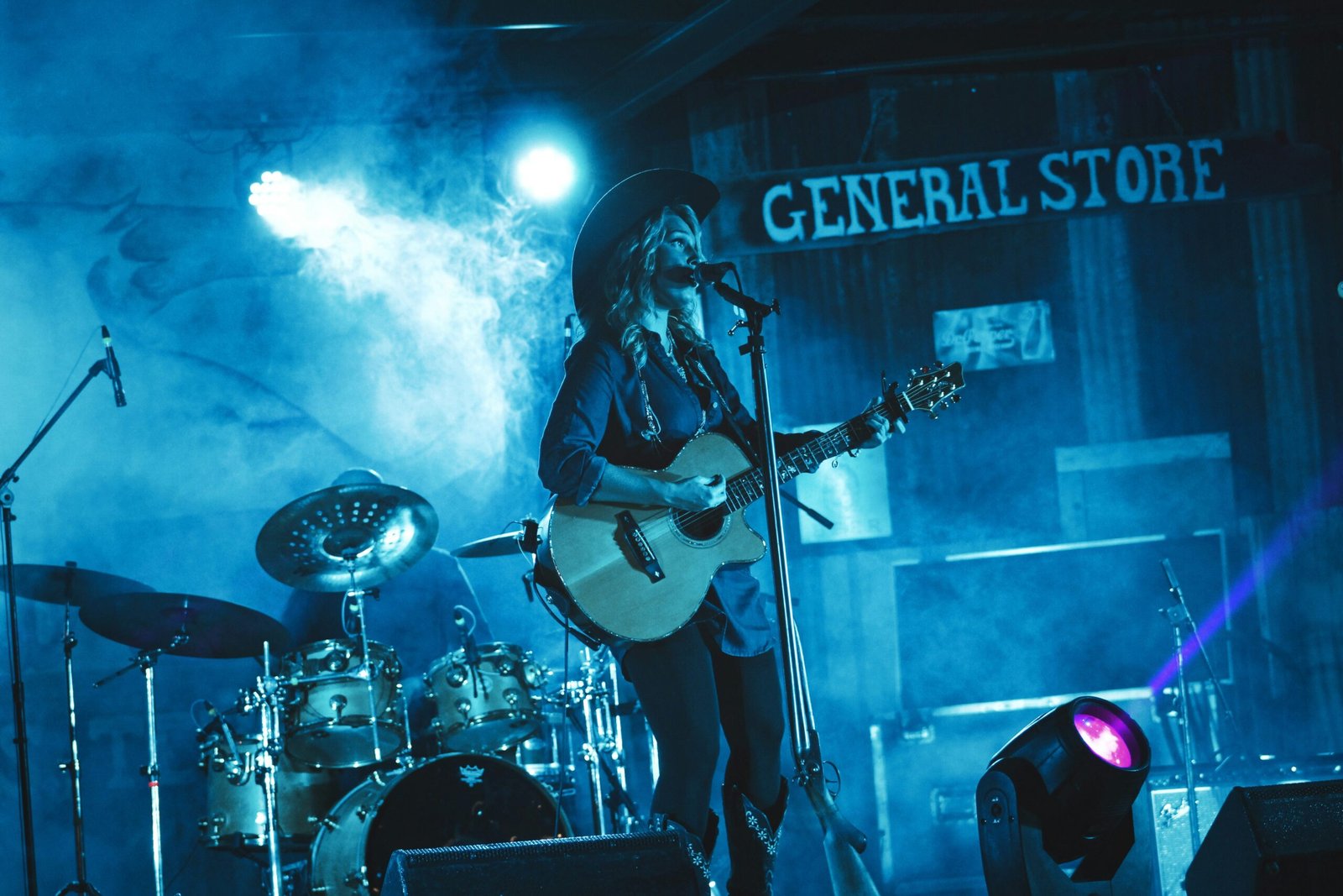 Country roots festival Female country singer playing an electric guitar and singing into a microphone. She is on a stage with drummer drumming on a set of drums