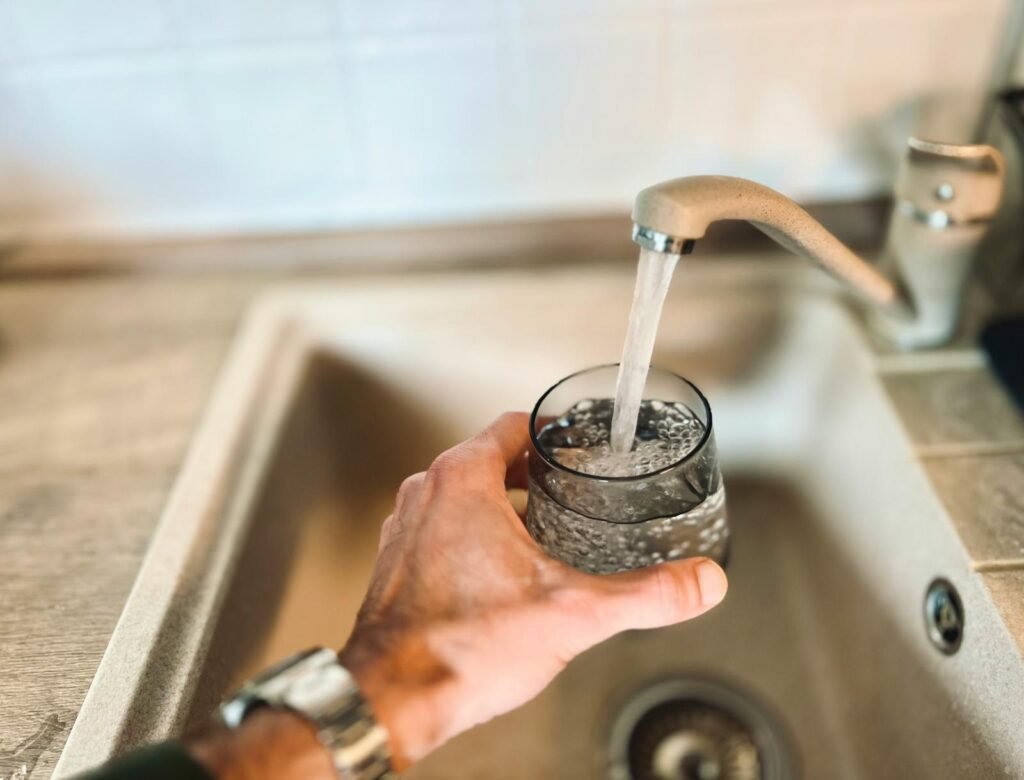 A hand holding a bottle under a running tap to fill it with water.