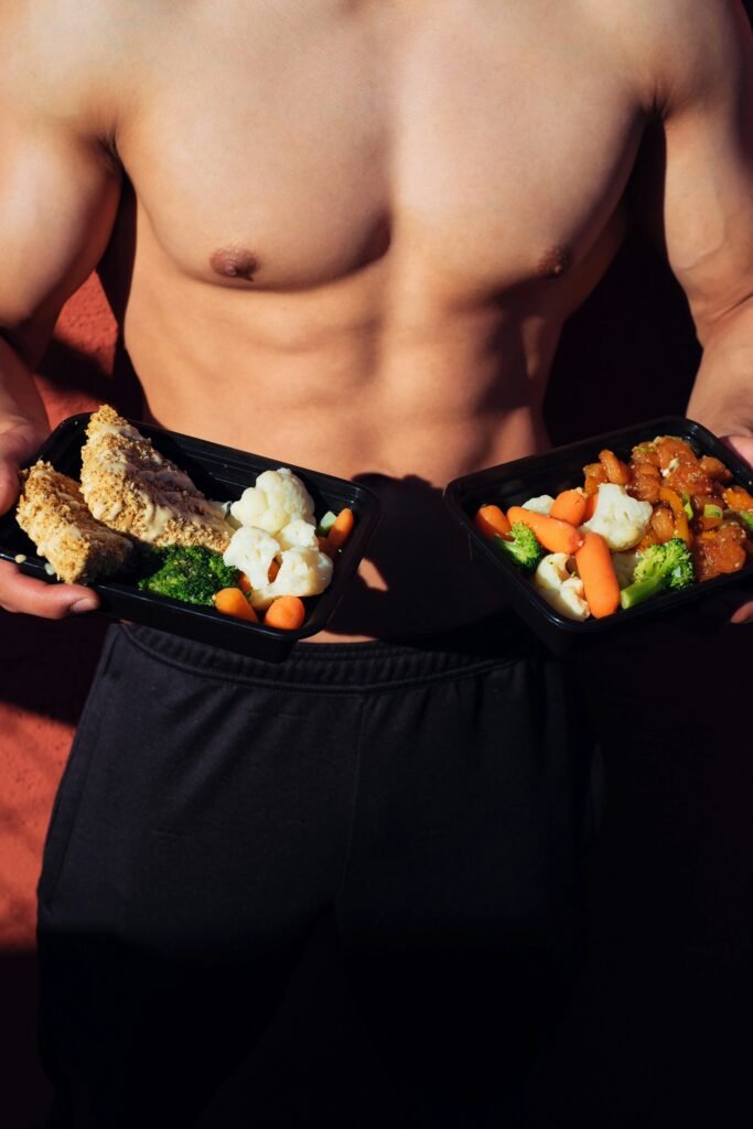 A muscular person holding a container with a balanced healthy meal of protein, healthy fats and vegetables.